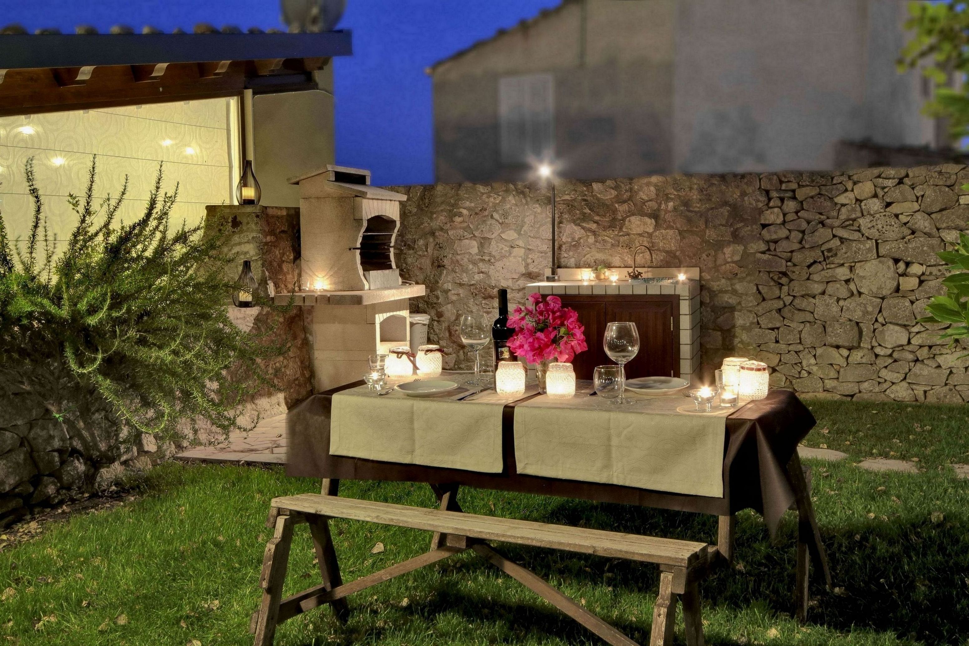 Tavolo apparecchiato all'aperto con candele e una bottiglia di vino.