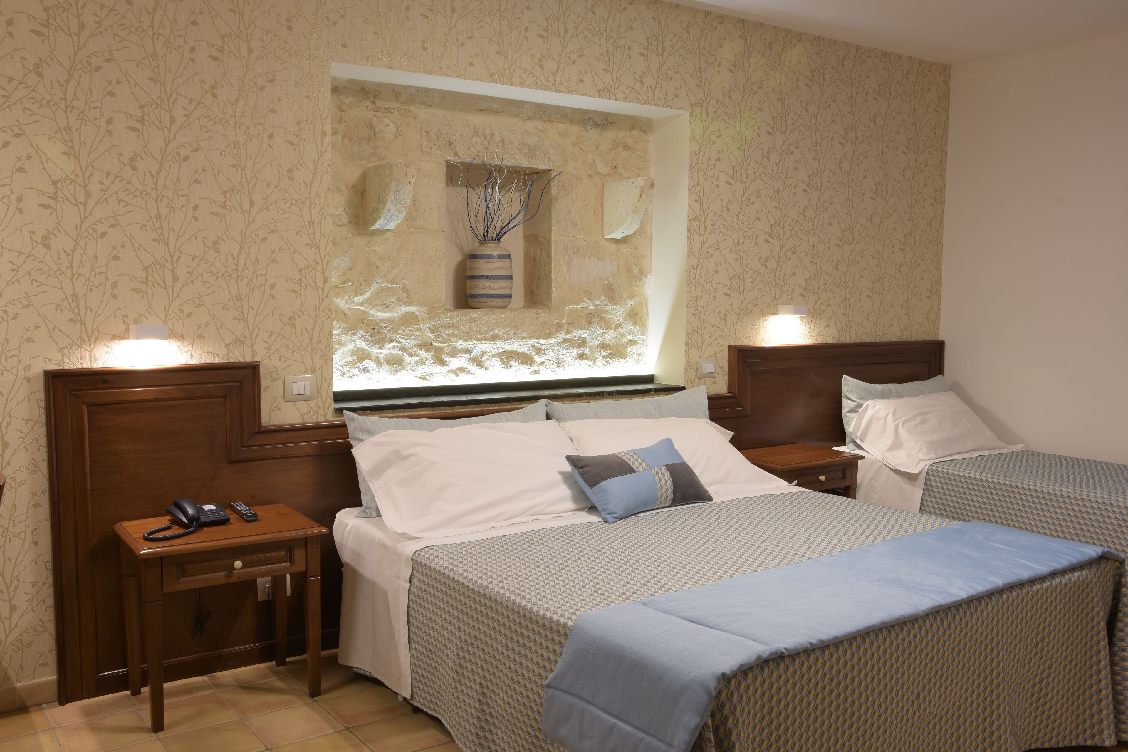 A hotel room with two beds, a small bedside table with a phone, and a wall-mounted vase.