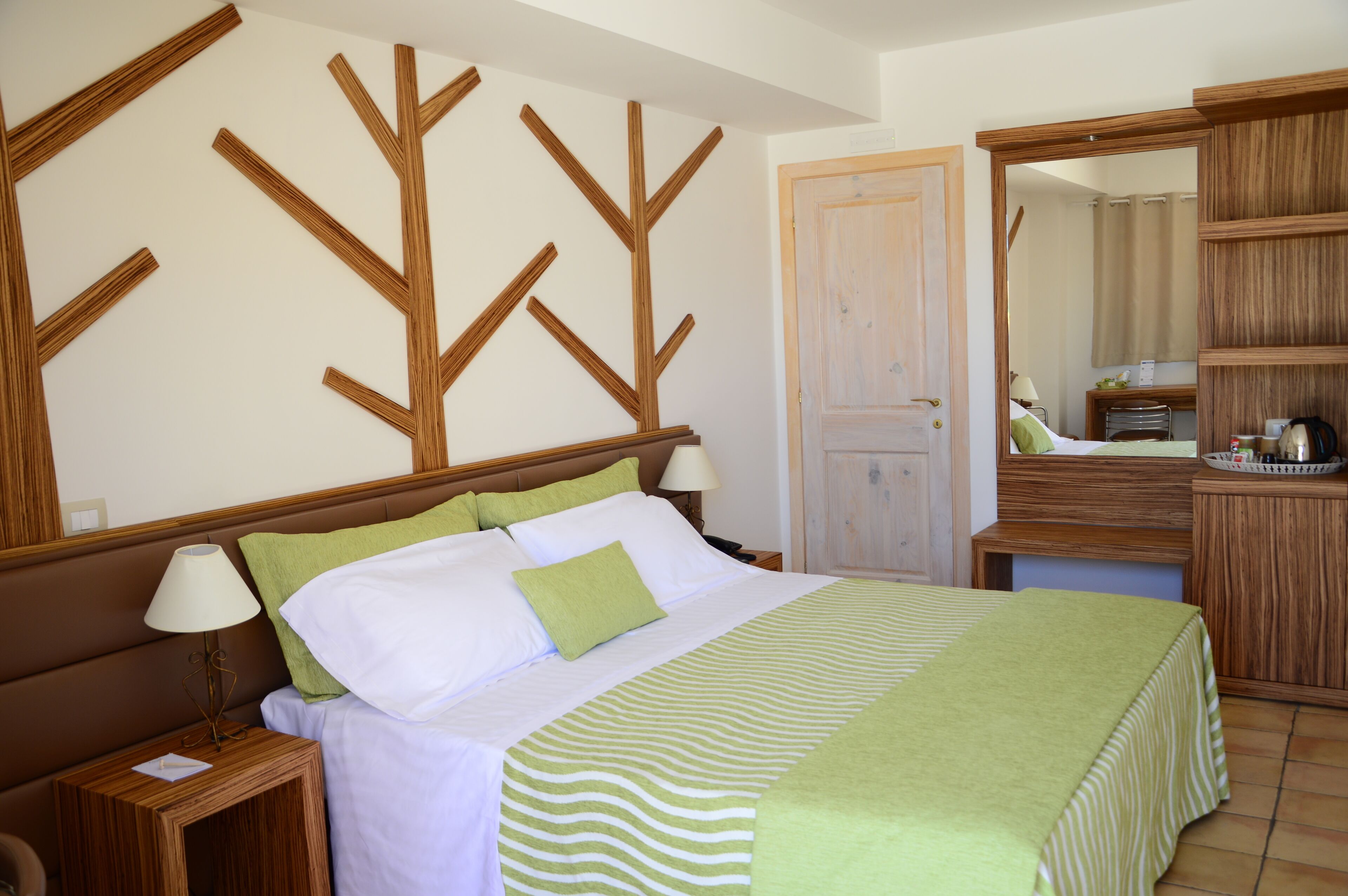 Una cama bien hecha con colcha a rayas, una mesita de noche con lámpara y un cabecero de madera con diseño de árbol.