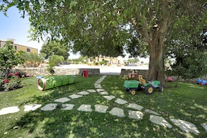 Un jardín con un sendero de piedra, un árbol y un tractor verde.