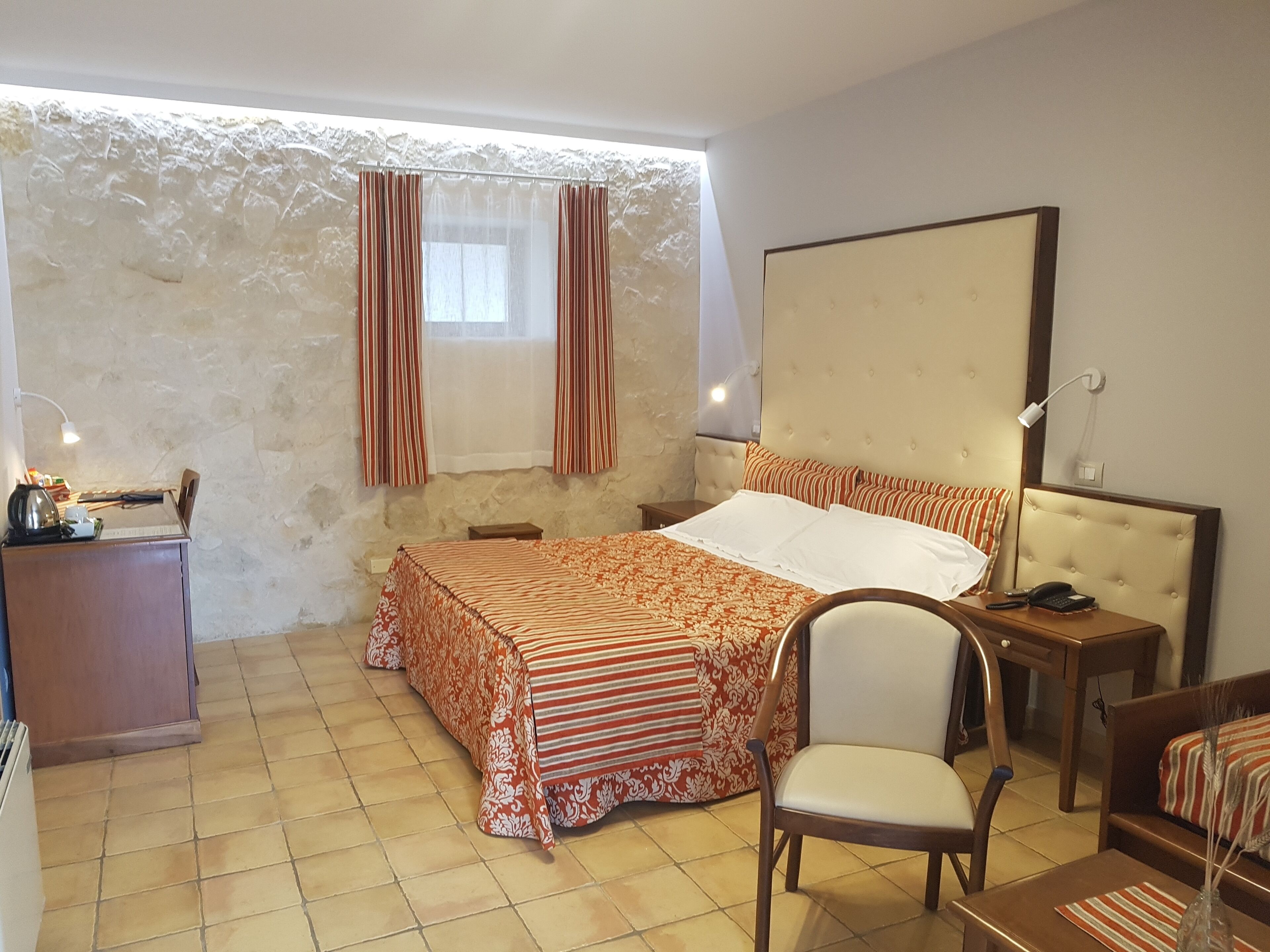 Ein Schlafzimmer mit einem Bett, einem Sessel, einem Schreibtisch, einer Lampe und einem Spiegel.