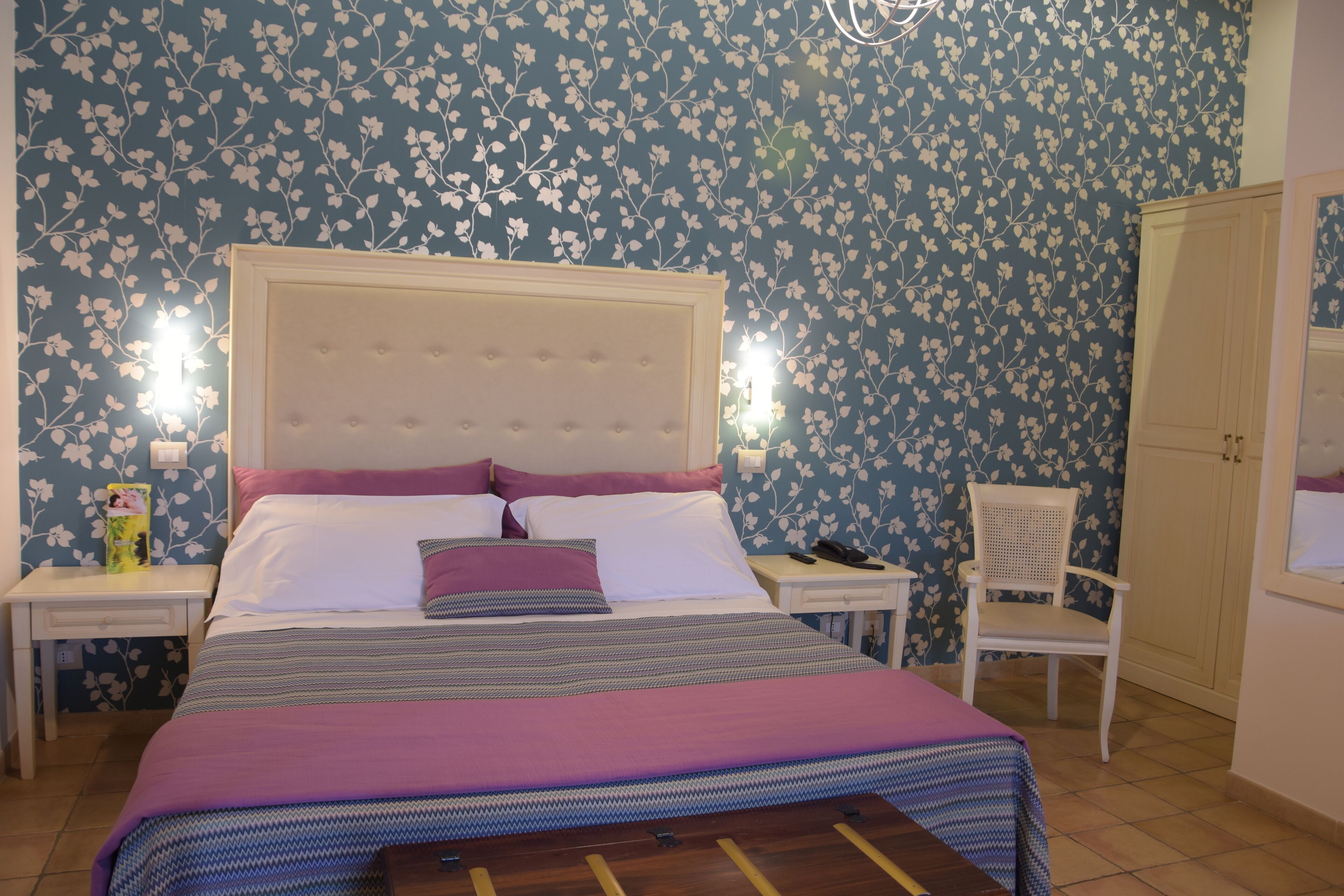Un dormitorio con una cama, mesitas de noche, una silla y un armario.