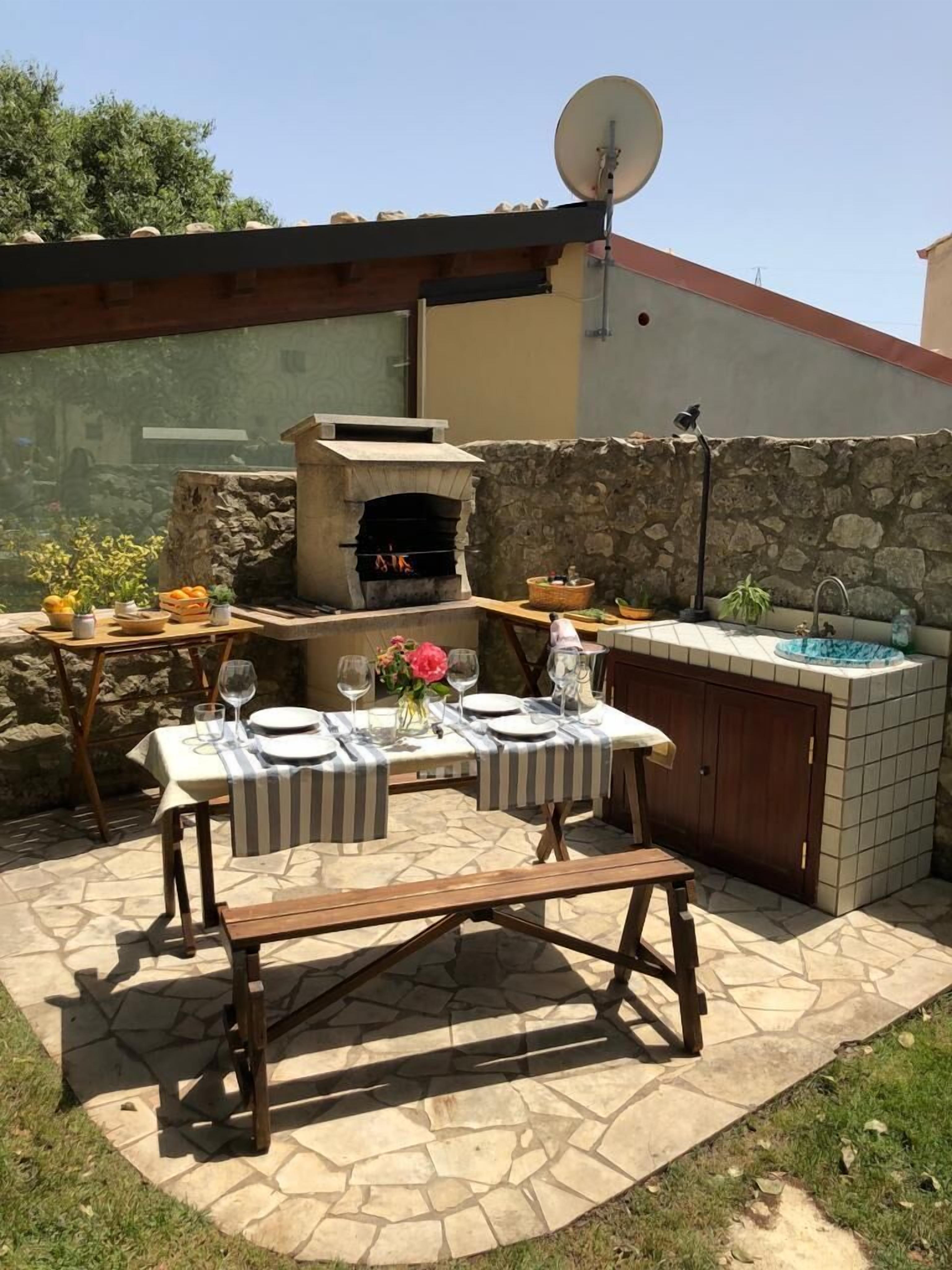 An outdoor patio with a stone table, a brick oven, and a stone sink.