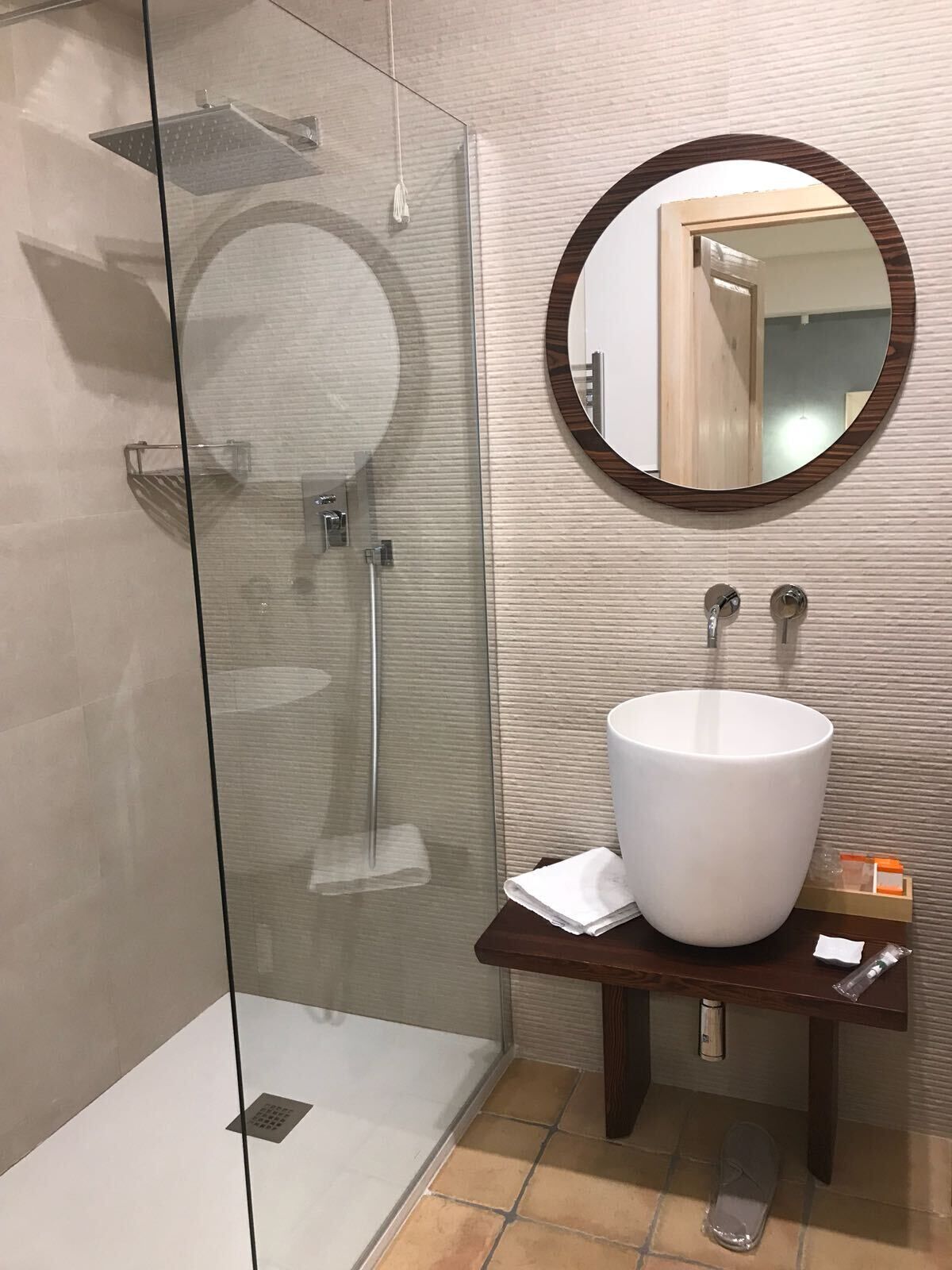 A modern bathroom with a glass-enclosed shower, a large white sink, and a wooden-framed mirror.