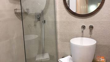A modern bathroom with a glass-enclosed shower, a large white sink, and a wooden-framed mirror.