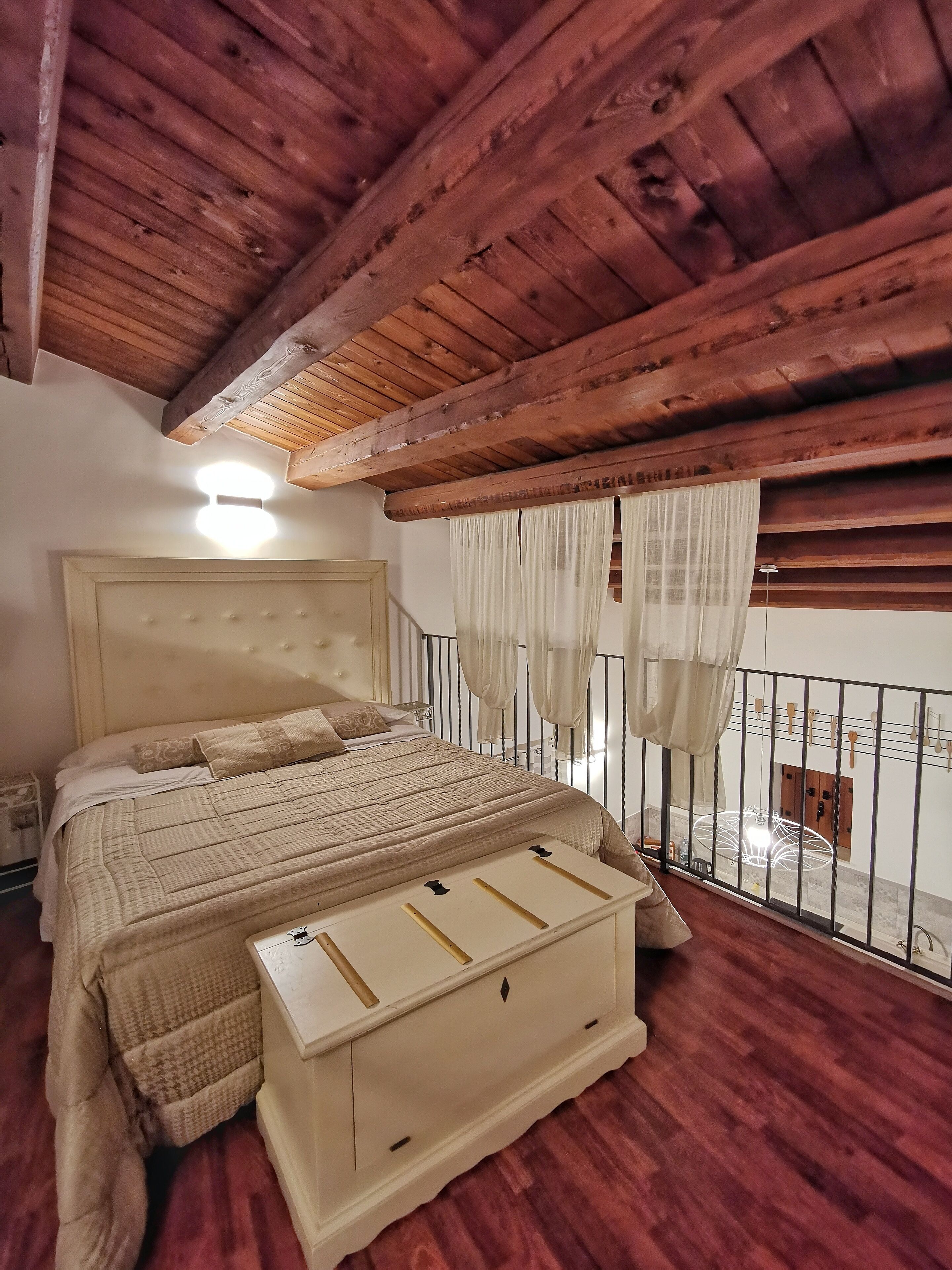 A bedroom with a wooden ceiling, a bed with a headboard, a bedside table, and a window with curtains.