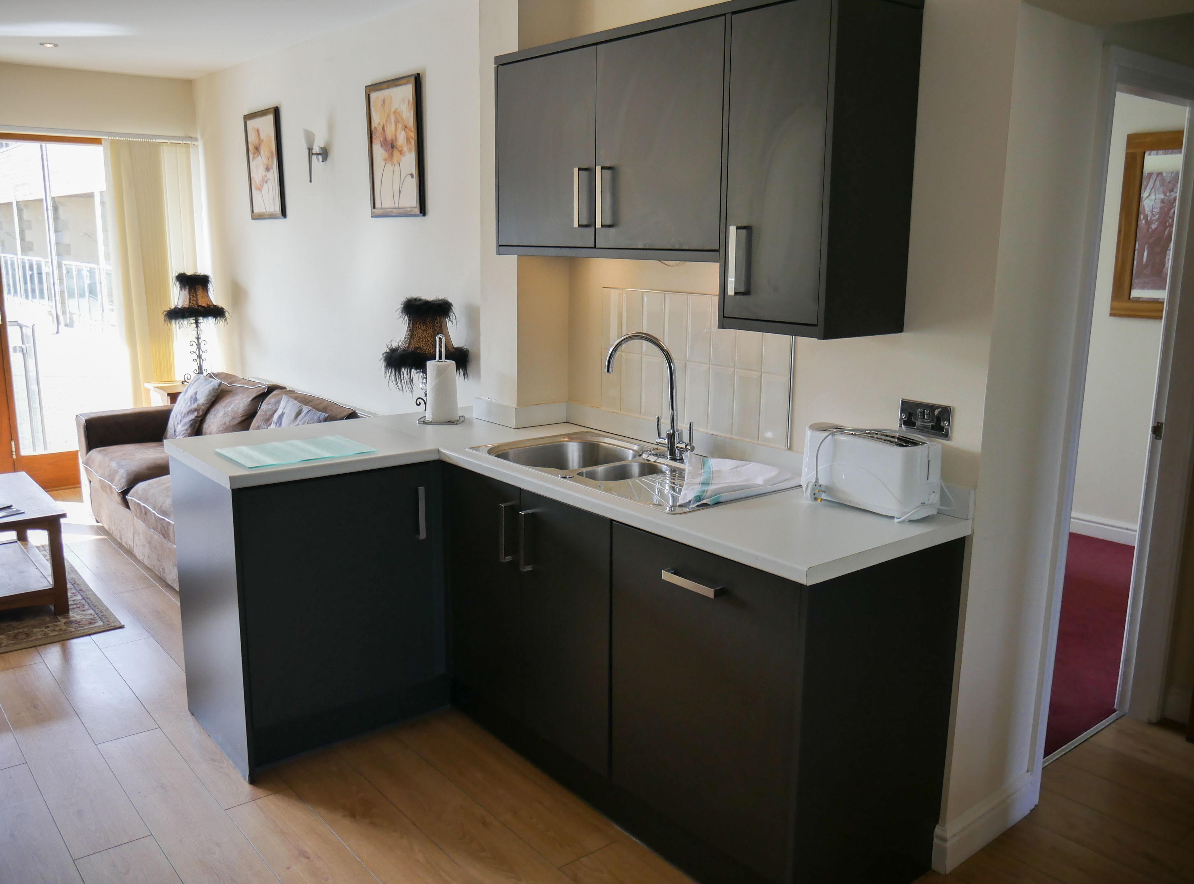 A compact kitchen with dark cabinets, a sink, and a toaster. There is a small island with a countertop and a chair.