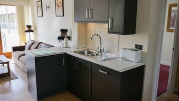 A compact kitchen with dark cabinets, a sink, and a toaster. There is a small island with a countertop and a chair.