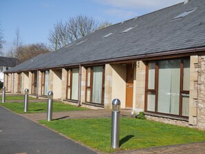 A row of rooms with large windows, a stone facade, and a paved pathway.