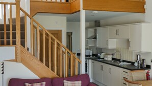Una casa de varios niveles con una escalera de madera, un sofá púrpura, una mesa de centro de madera y una zona de cocina.