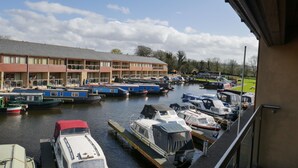 Un puerto deportivo con barcos amarrados, un edificio con varios balcones y una zona verde al fondo.