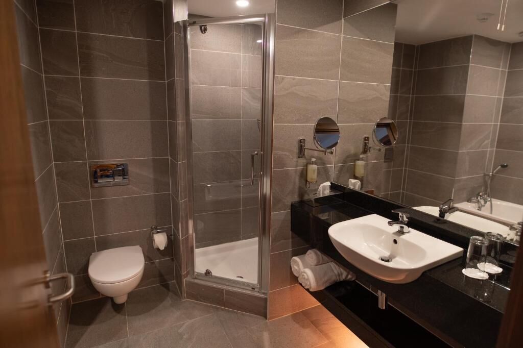 A modern bathroom with a glass-enclosed shower, a white toilet, a sink, and a large mirror.