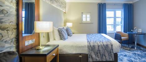 A hotel room with a bed, a desk, a chair, a mirror, and a window with curtains.