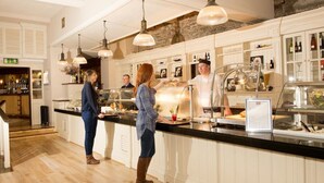 A modern kitchen with a bar area, featuring a counter with a glass display case, hanging pendant lights, and a stone accent wall. - Riverside Park Hotel and Leisure Club (Enniscorthy)