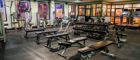 A gym with various exercise equipment including benches, dumbbells, and cardio machines.