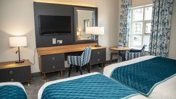 A hotel room with two beds, a desk, a chair, a TV, and a window with curtains.