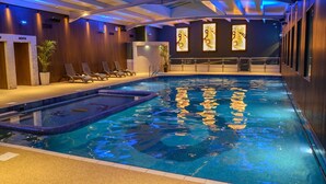 An indoor swimming pool with a tiled edge, lounge chairs, and a wall with artwork. - Riverside Park Hotel and Leisure Club (Enniscorthy)