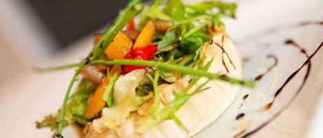 Une vue rapprochée d’un plat gastronomique composé de divers légumes et de différentes sortes de verdure, servi sur une assiette en verre transparent et agrémenté d’un filet de sauce.