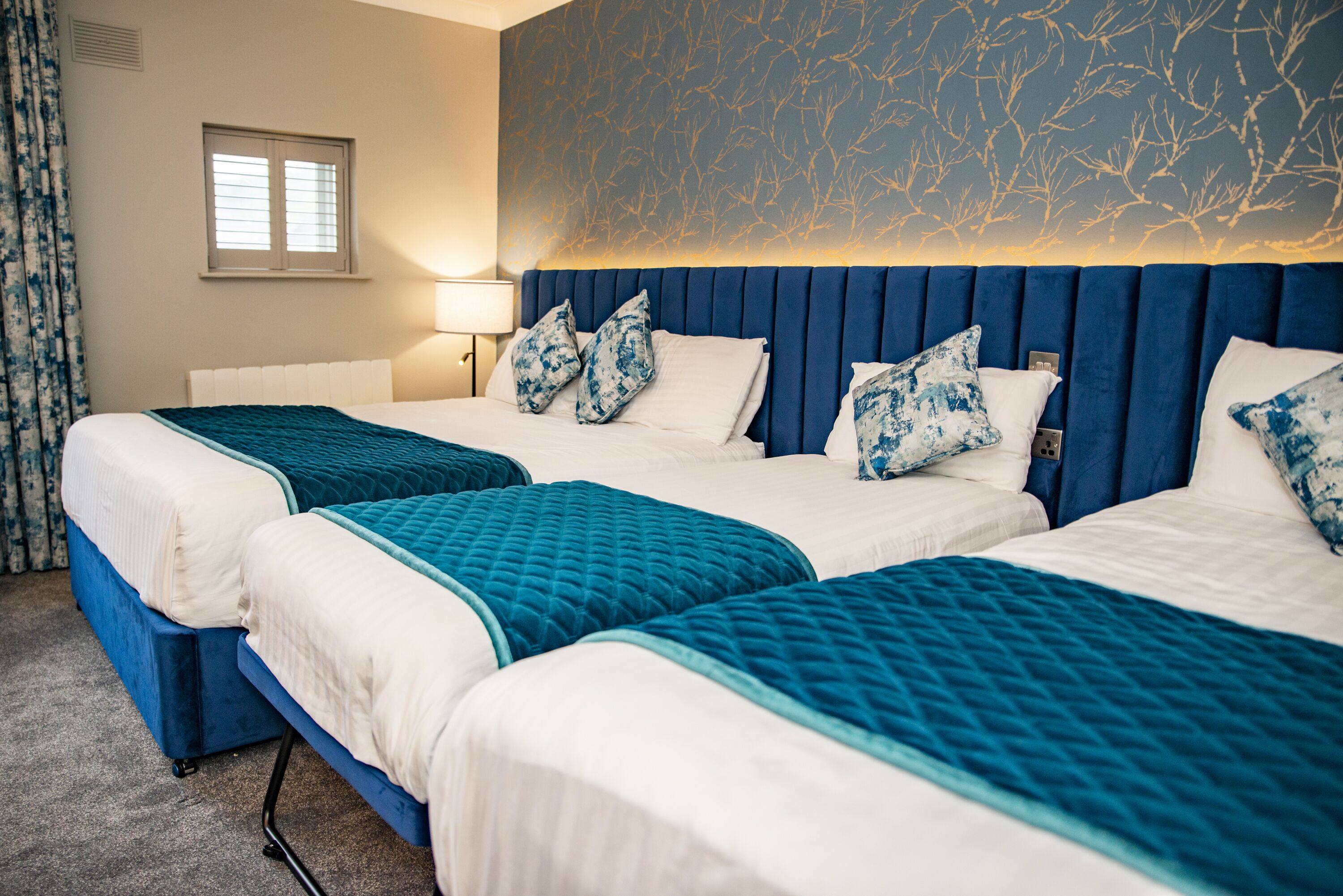 A hotel room with two beds, a window, and a wall with a tree pattern.