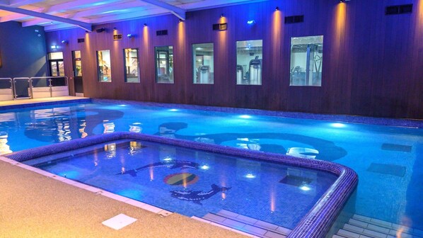 Una piscina interior con borde de azulejos, un jacuzzi en el centro y una pared de madera con ventanas.