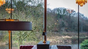 A room with a view of a river and trees, featuring two leather sofas and a table. - Riverside Park Hotel and Leisure Club (Enniscorthy)