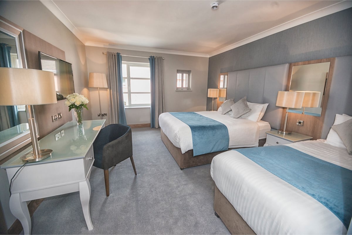 A hotel room with two beds, a desk, a chair, a TV, and a window with curtains.