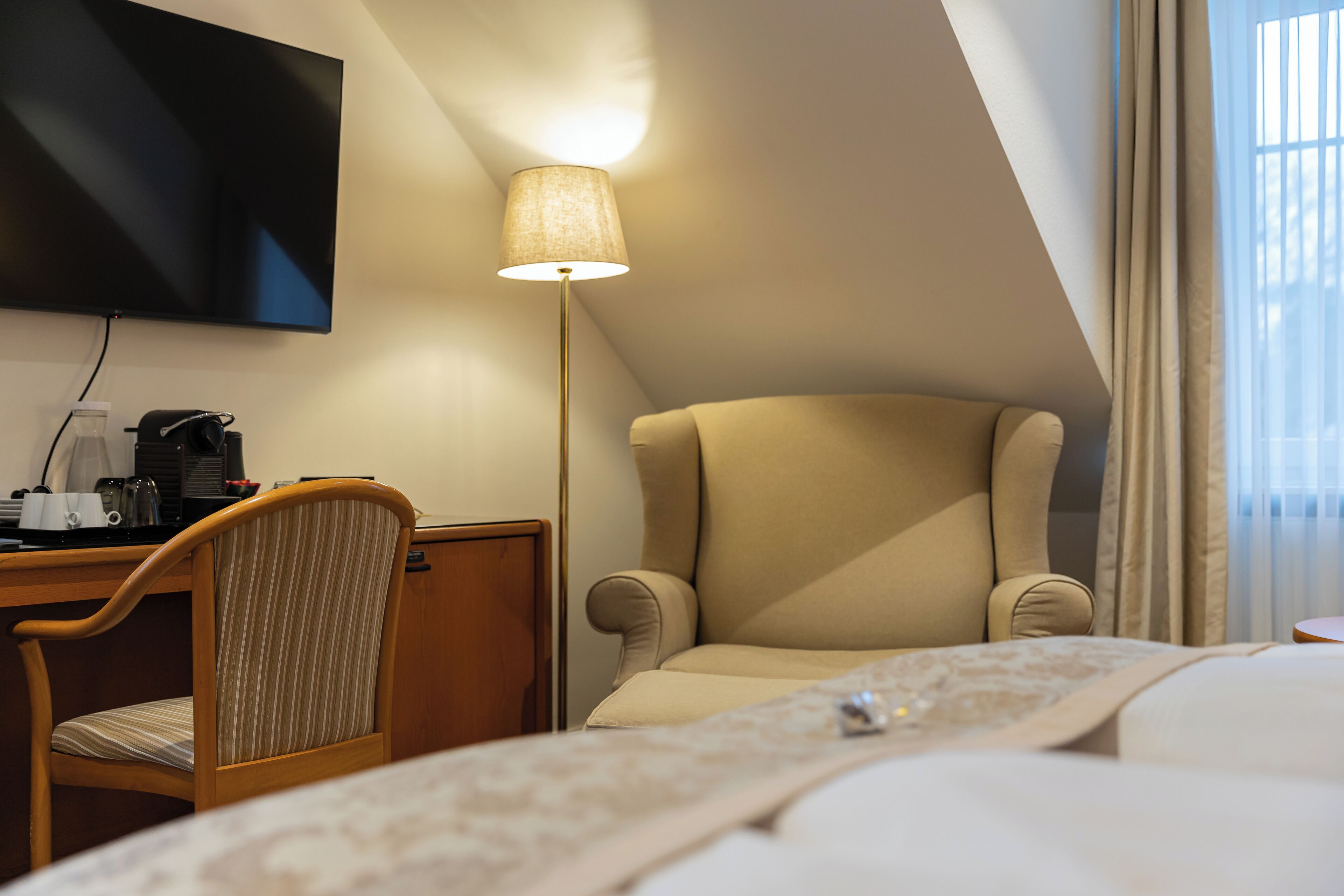 Habitació d'hotel amb un llit, una taula de treball amb una cadira, un televisió de pantalla plana, una làmpada i una finestra amb cortines.