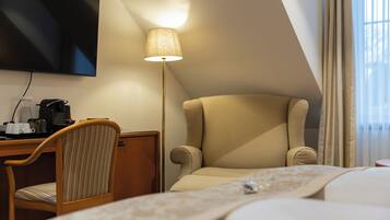 A hotel room with a bed, a desk with a chair, a flat-screen TV, a lamp, and a window with curtains.