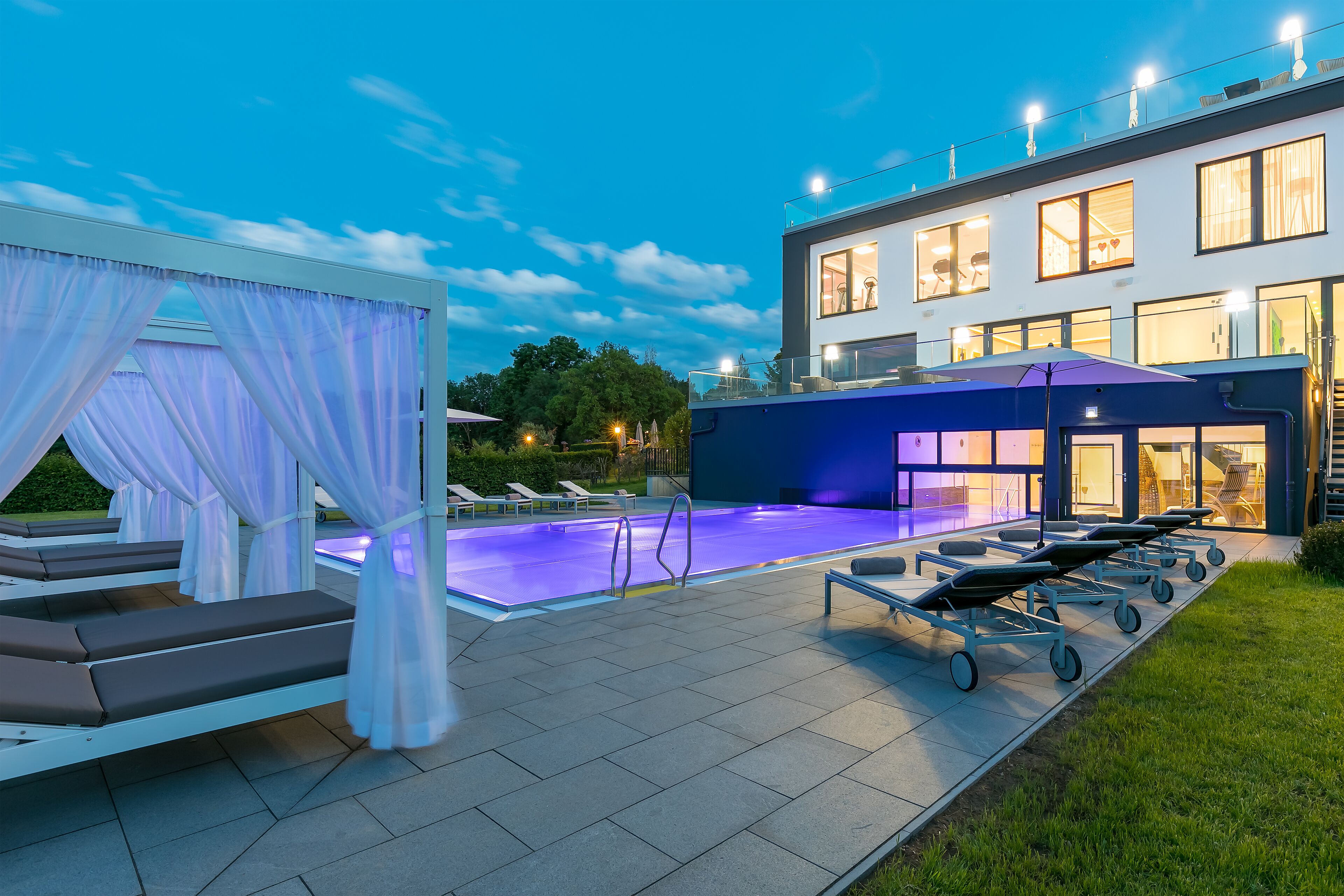 A modern outdoor pool area with lounge chairs, a canopy, and a building with large windows.