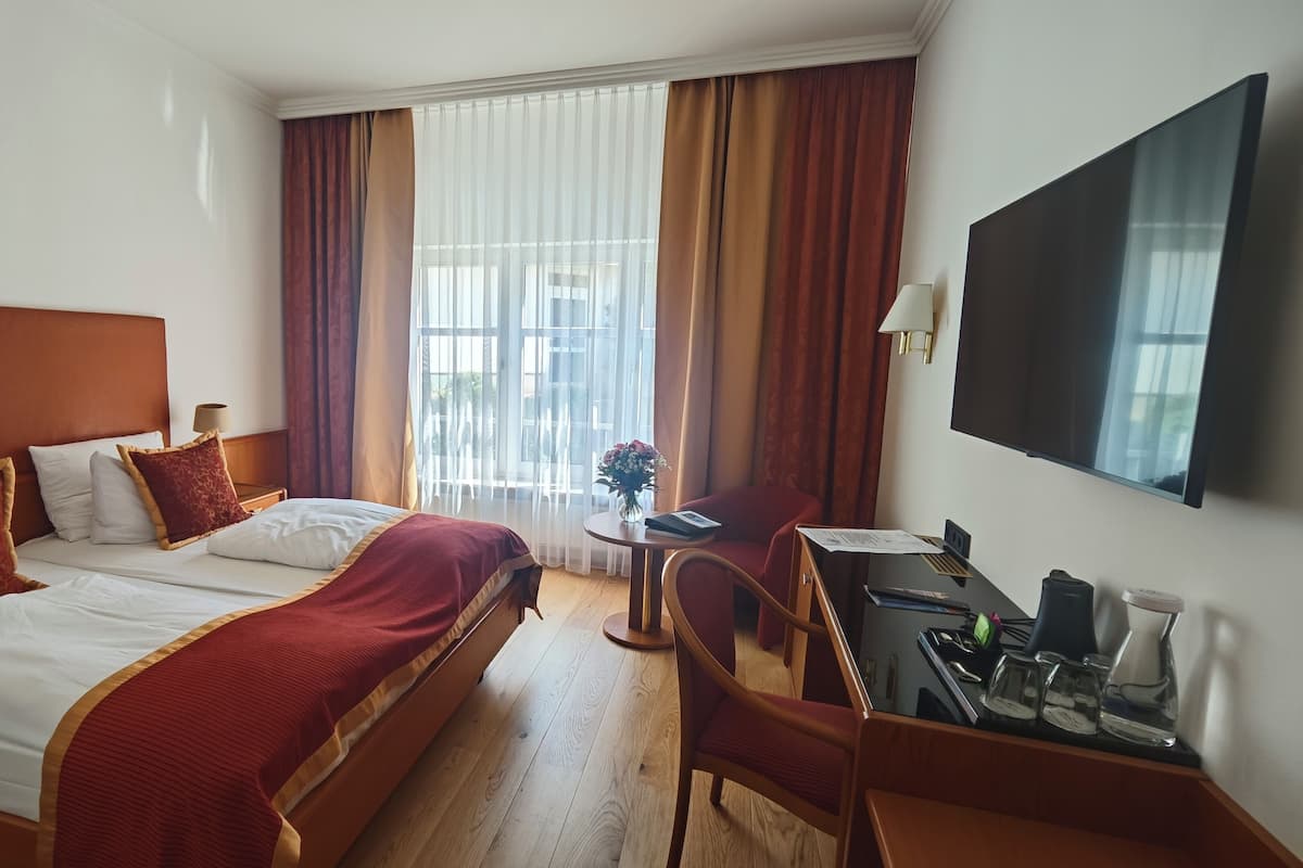 A hotel room with a large bed, a desk with a chair, a TV, and a window with curtains.