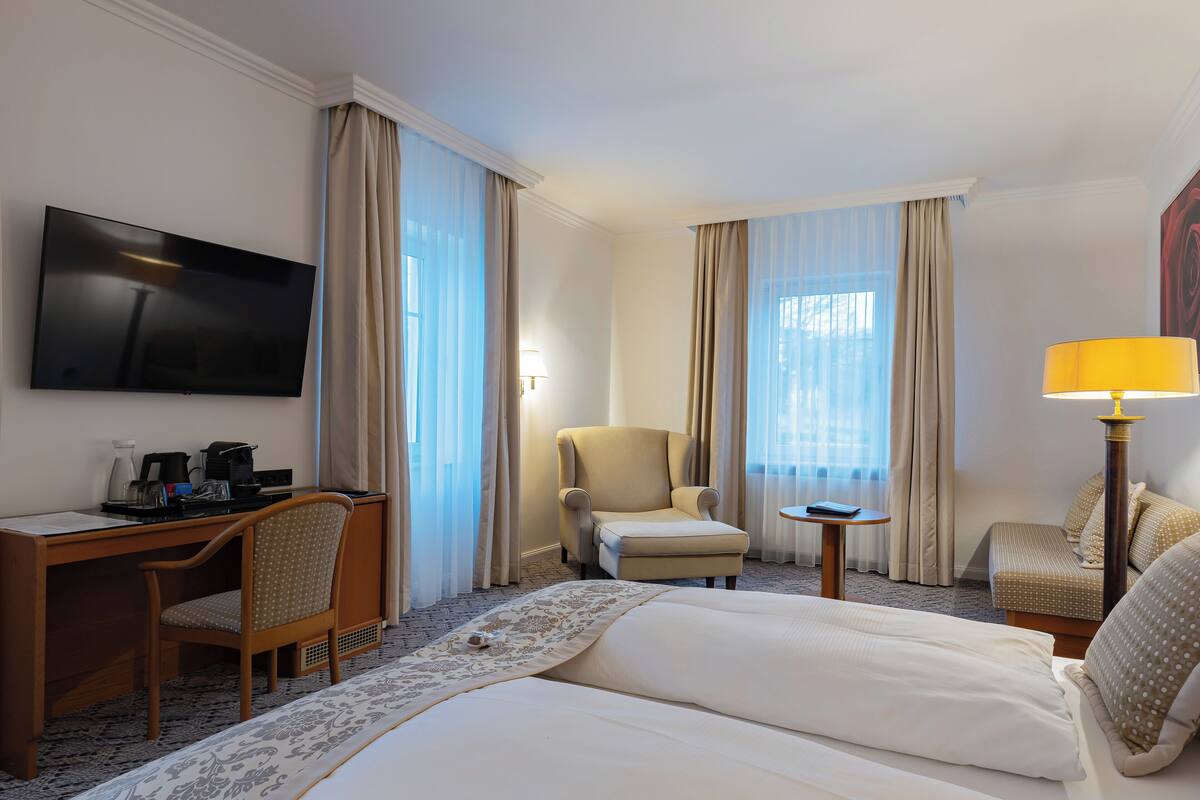 A hotel room with a bed, a desk, a chair, a TV, and a lamp.