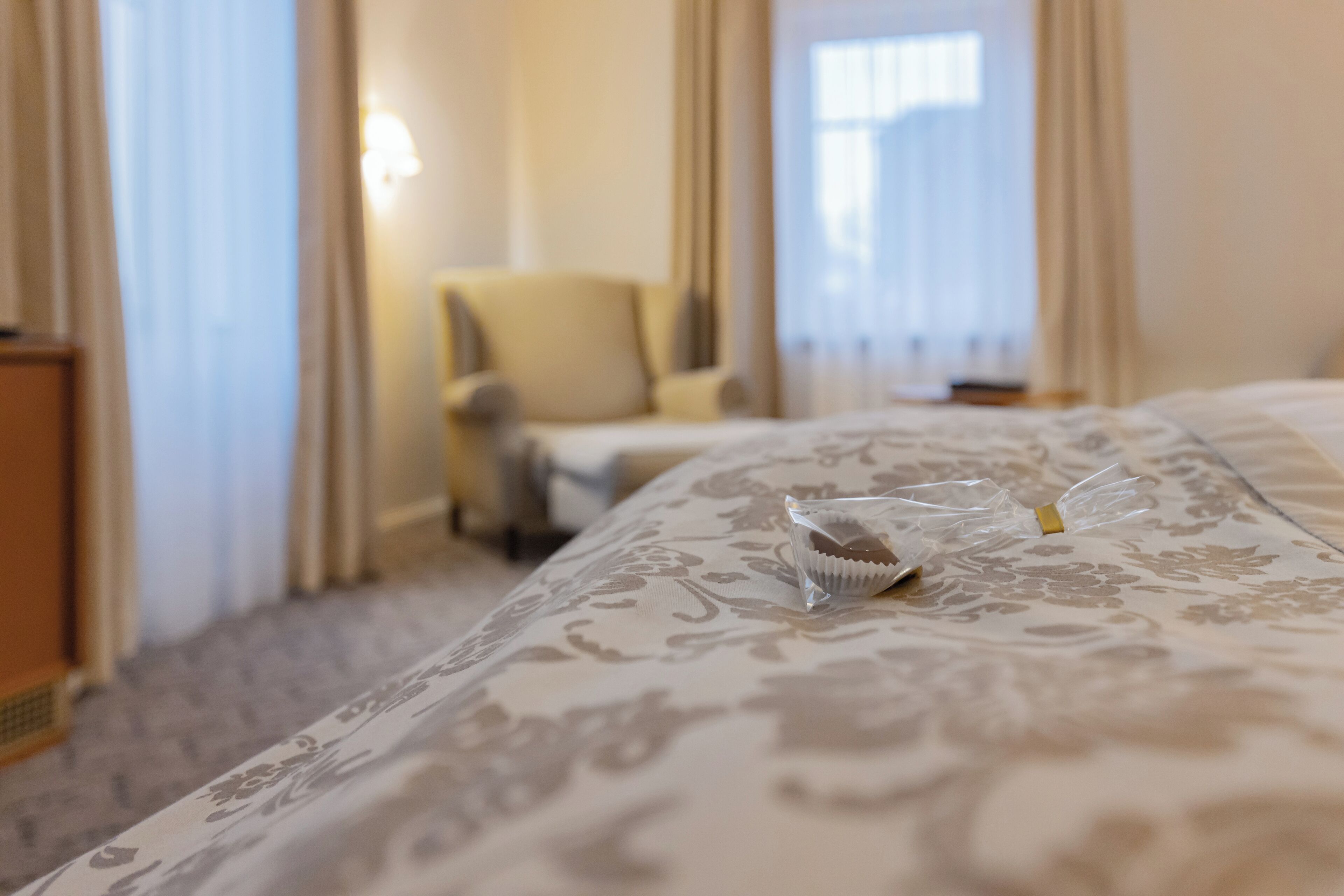 A hotel room with a bed, a chair, and a window with curtains.