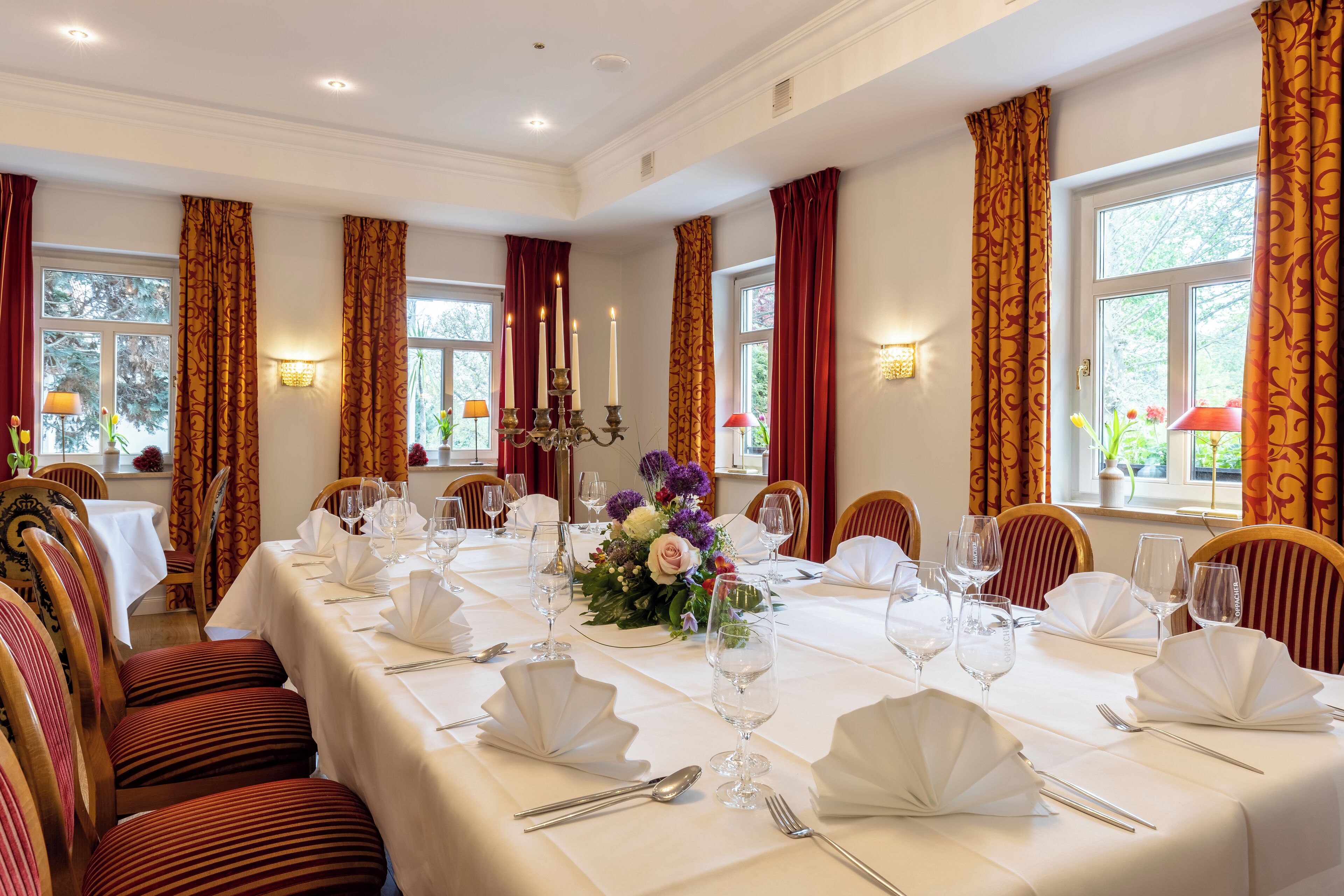 A dining room with a long table set for a formal meal, surrounded by chairs.