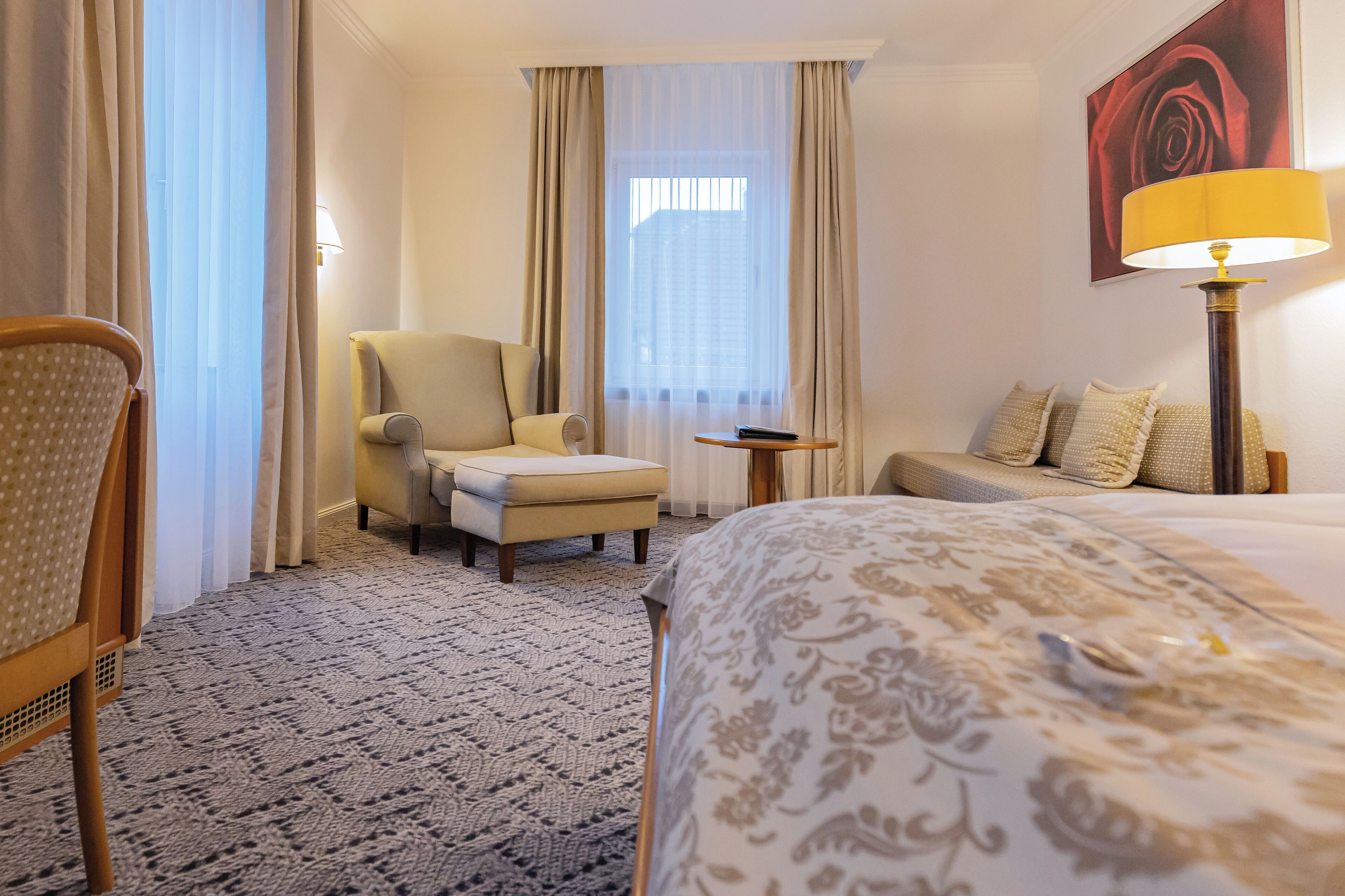 A hotel room with a bed, a chair, a small table, and a lamp.