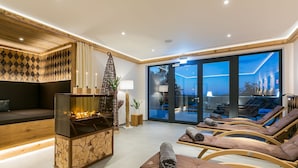 A modern living room with a fireplace, lounge chairs, and a large glass door leading to an outdoor area. - Romantik Hotel Schwanefeld (Meerane)