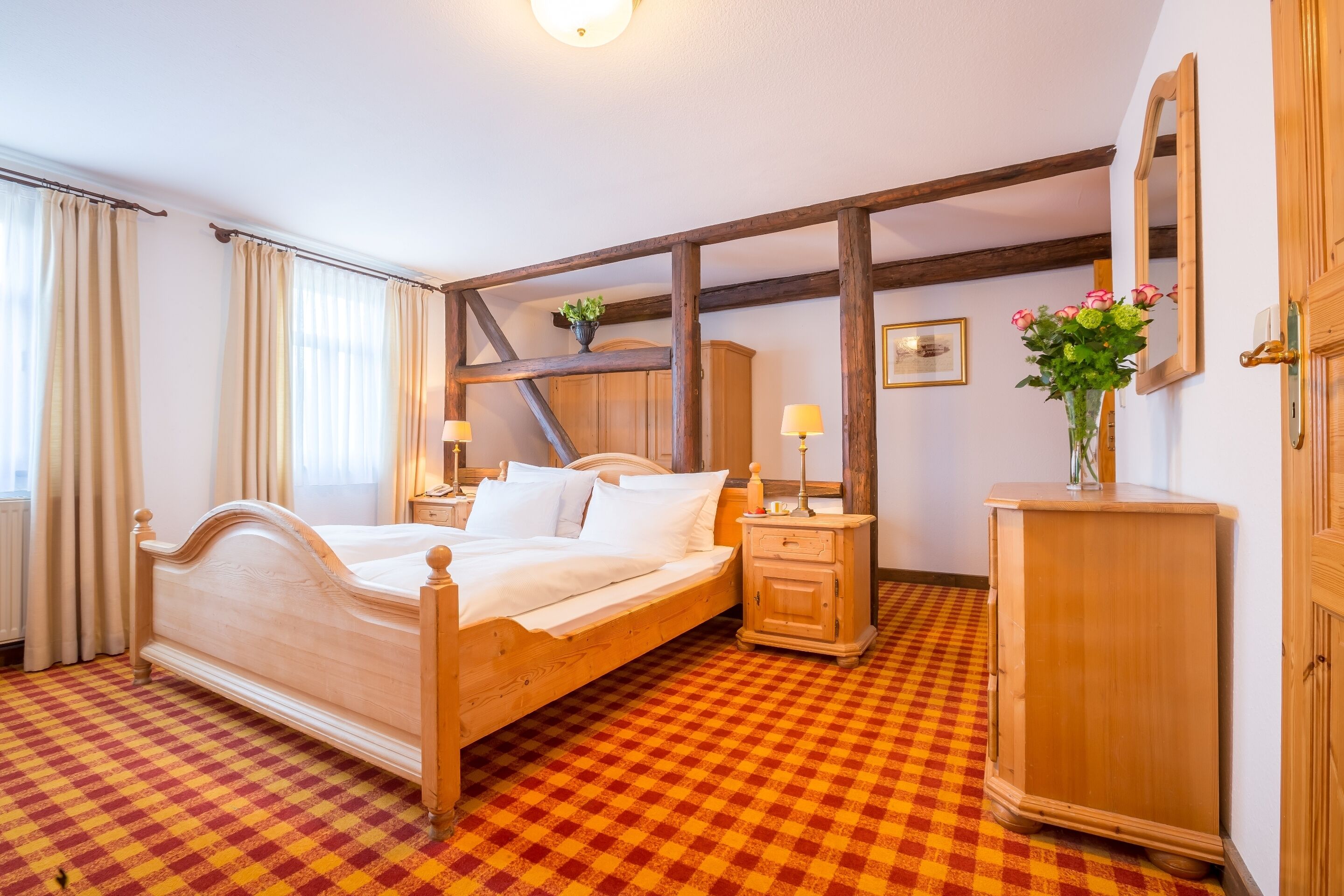 A hotel room with a wooden bed, a checkered floor, a nightstand, a dresser, and a mirror.