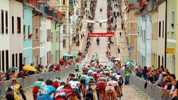 Una calle adoquinada flanqueada por edificios coloridos, una multitud de ciclistas y espectadores siguiendo una carrera de ciclismo.