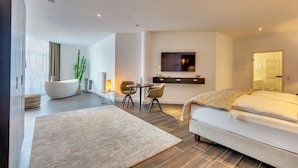 A modern hotel room with a large bed, a seating area with chairs, a flat-screen TV mounted on the wall, and a large window with curtains. - Romantik Hotel Schwanefeld (Meerane)