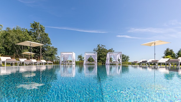 A clear blue pool with white sun loungers and umbrellas, surrounded by trees. - Romantik Hotel Schwanefeld (Meerane)