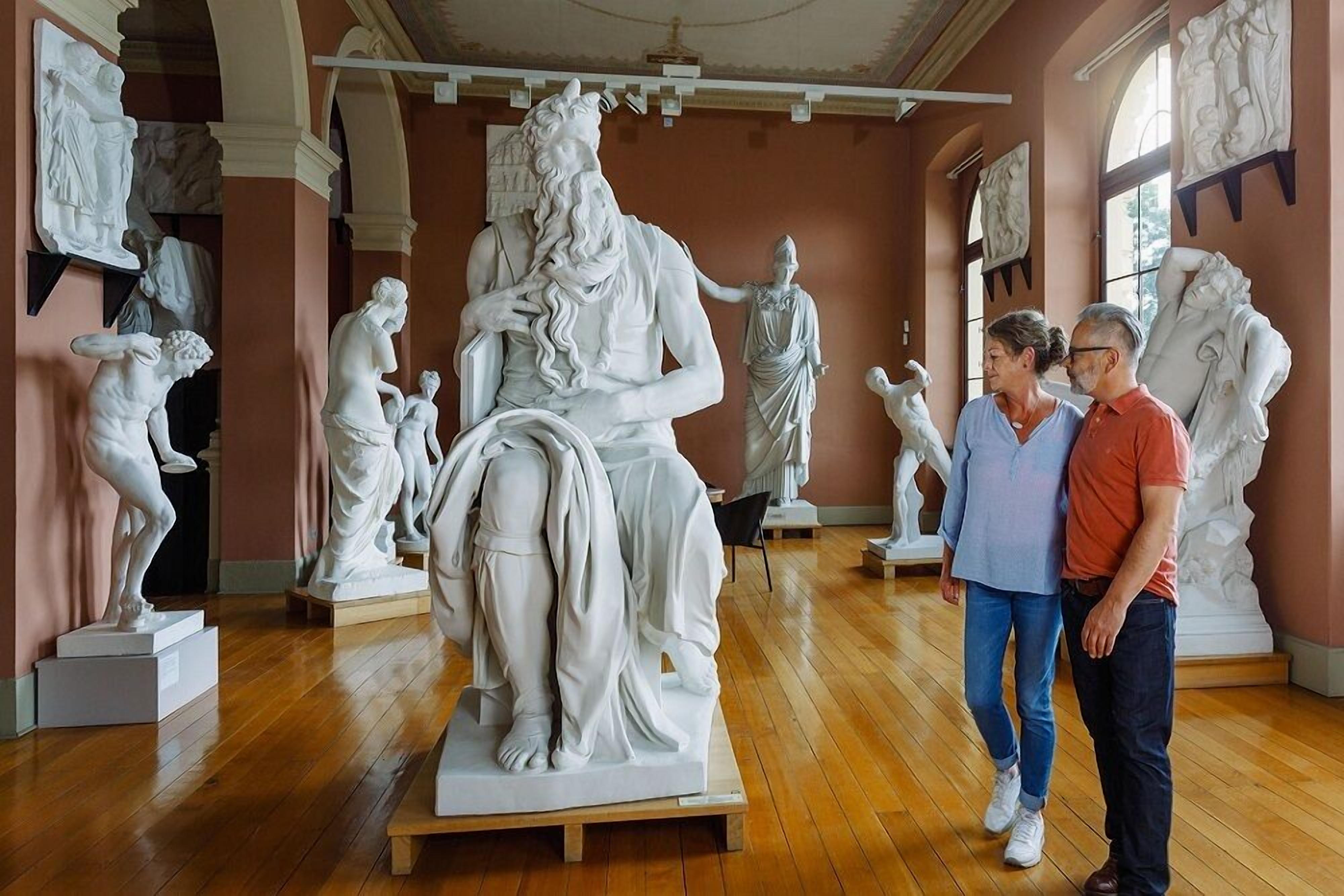 L’intérieur d’un musée, avec des sculptures en marbre sur des piédestaux, un plancher en bois et un plafond élevé orné de moulures décoratives.