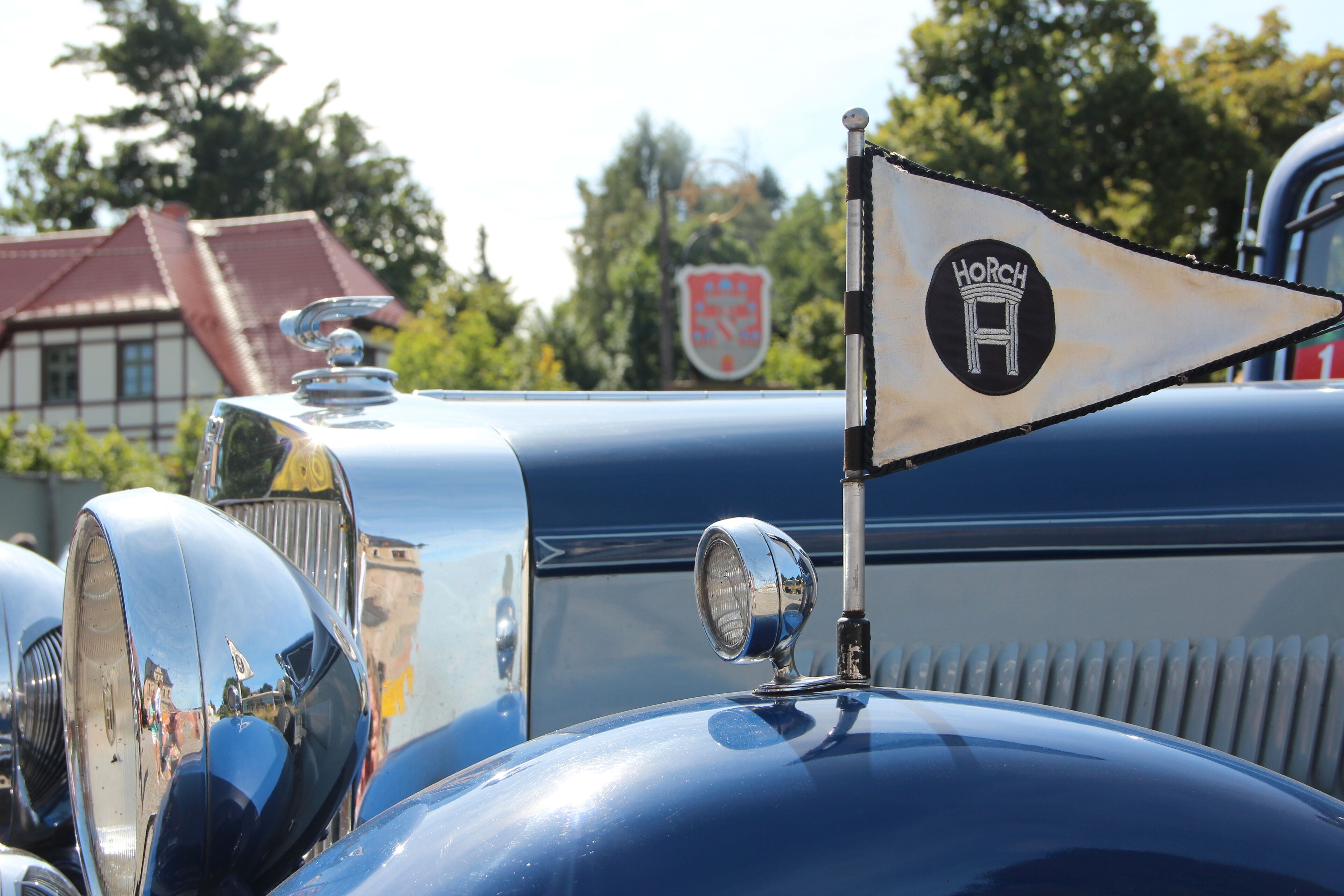 A vintage car with a prominent emblem and a flag on the hood.