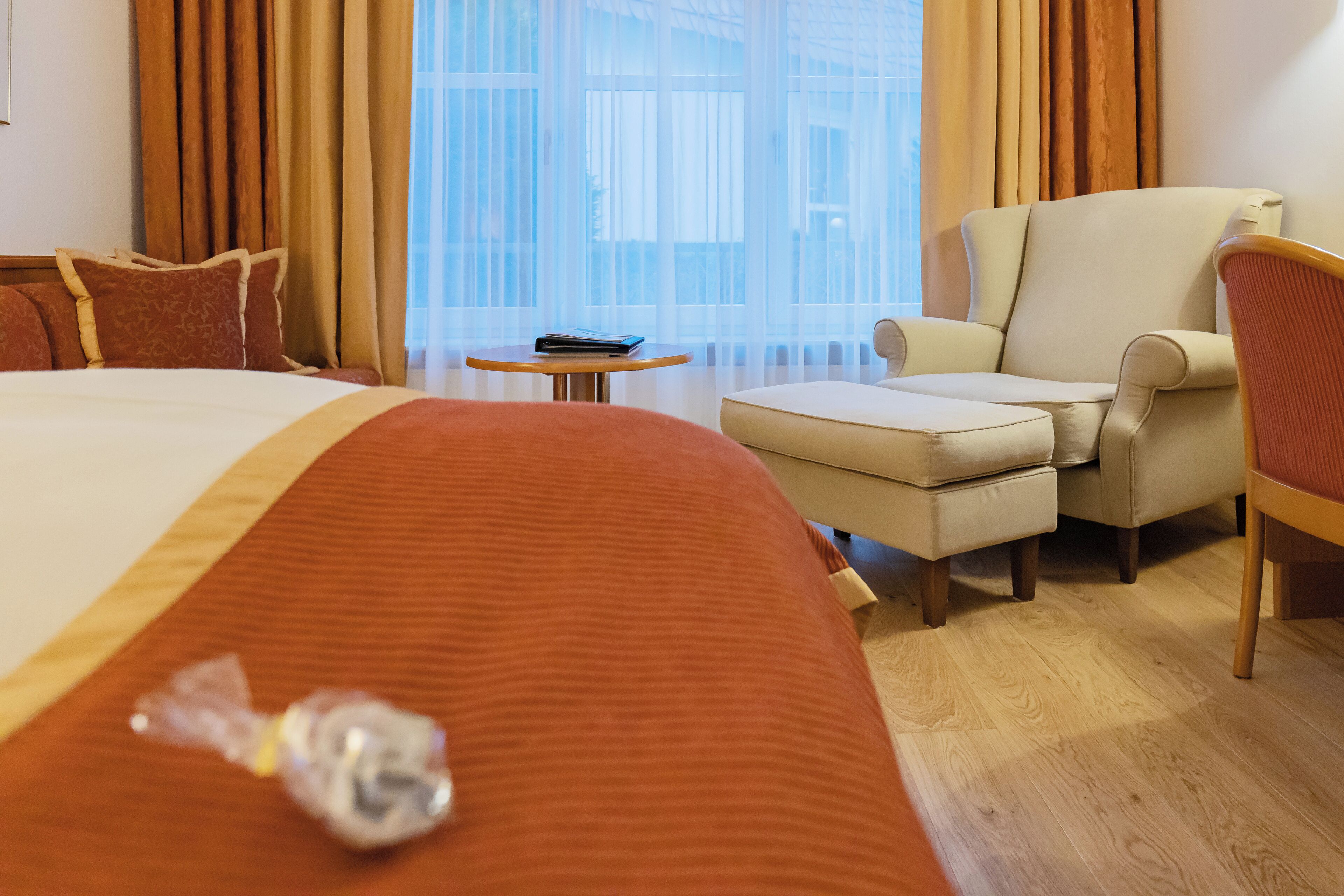 A hotel room with a large bed, a sofa, a chair, a small table, and a window with curtains.