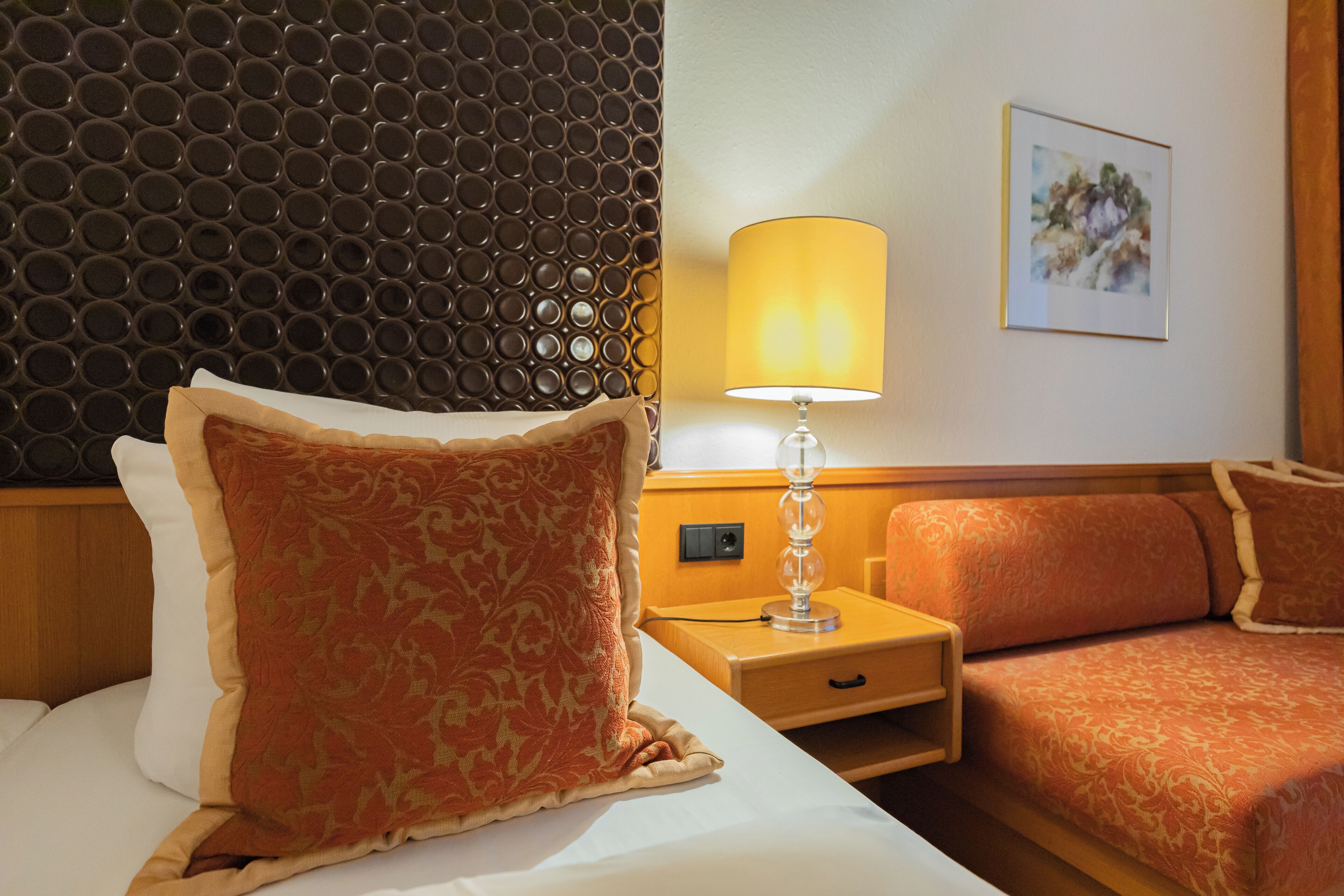A hotel room with a bed, a nightstand, a lamp, and a sofa.