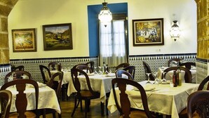 A restaurant with a high arched ceiling, wooden chairs, tables with white tablecloths, and tiled walls with artwork. - El Caballo Blanco (Osuna)