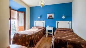 A bedroom with two beds, a small bedside table, a nightstand, a chandelier, and a window with blinds. - El Caballo Blanco (Osuna)