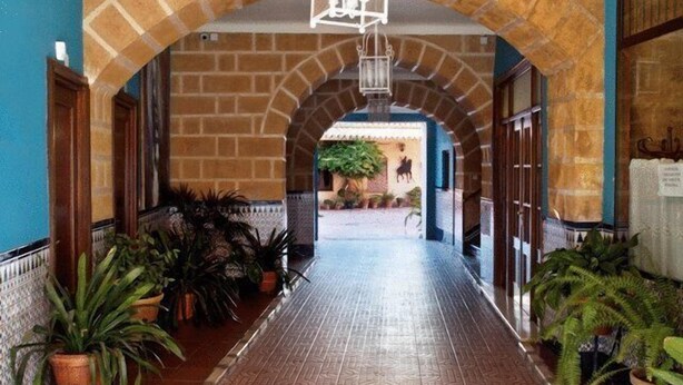 A hallway with a tiled floor, brick walls, and potted plants. - El Caballo Blanco (Osuna)