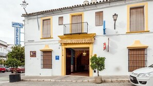 A white building with yellow trim, a sign for 'Hostal El Calallo Blanco', and a 'Hostal' sign. - El Caballo Blanco (Osuna)