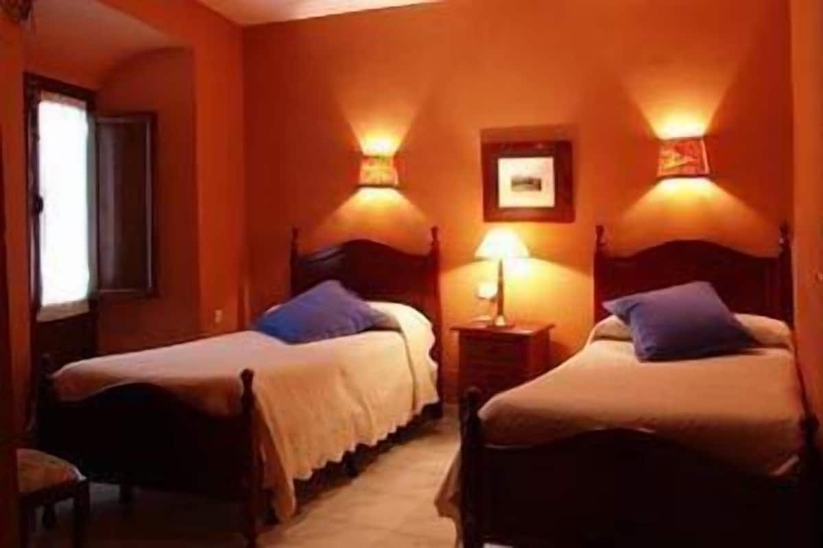 Una habitación de hotel con dos camas, una mesita de noche, una lámpara y un cuadro en la pared.