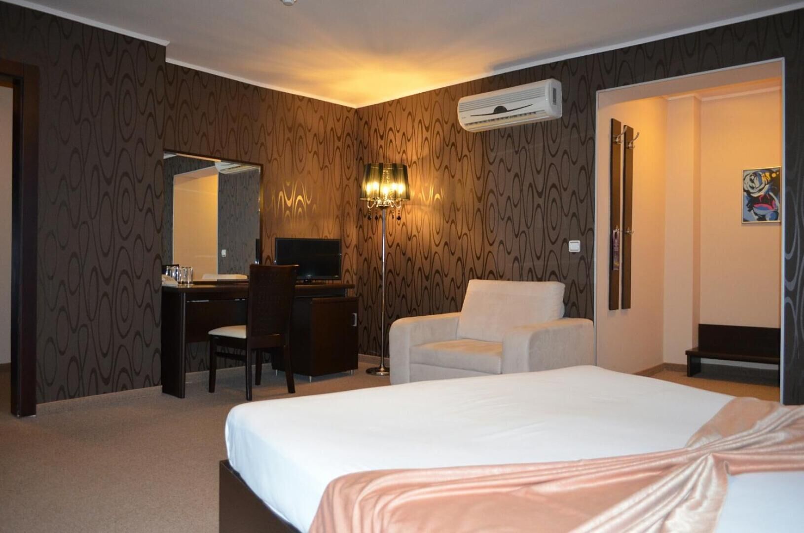 Ein Hotelzimmer mit einem Bett, einem Schreibtisch mit Stuhl, einer Couch, einer Klimaanlage und einem an der Wand befestigten Spiegel.