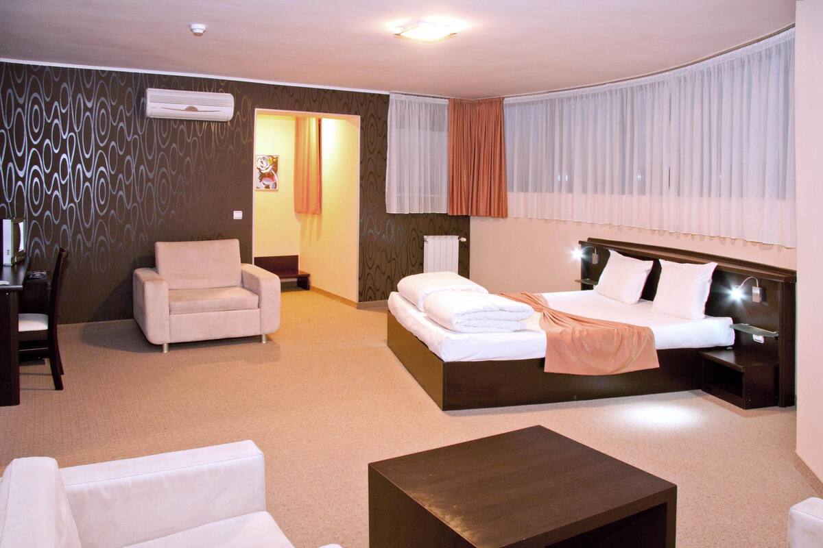 A hotel room with a bed, two chairs, a desk, and a coffee table.